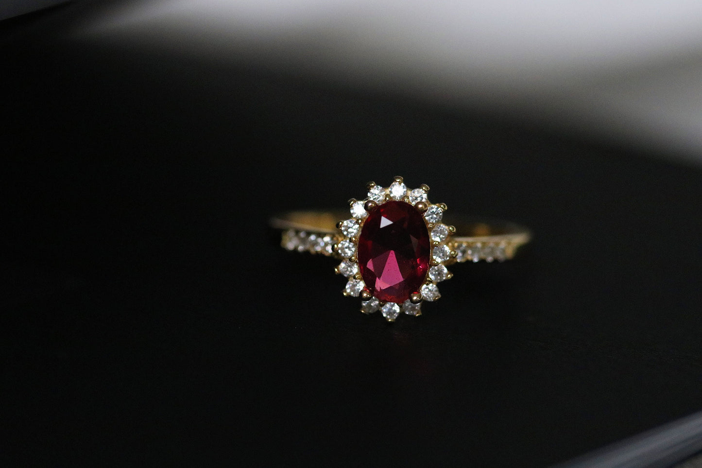 Gold Vermeil Ruby Halo Ring with CZ Accents featuring an elegant oval-cut red gemstone surrounded by a halo of sparkling cubic zirconia. Luxurious and durable, perfect for special occasions or everyday glamour.