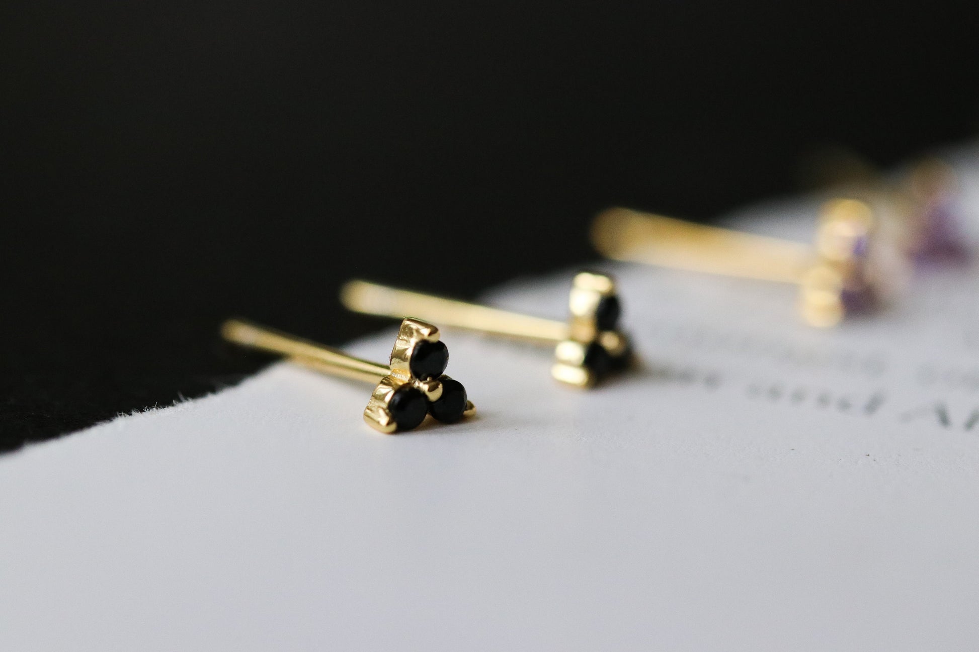 Shan&Co's Gold Vermeil CZ Black Shamrock Stud Earrings featuring a crystal black in a shamrock design, paired with Black Three Dot Earrings and Dainty Gold Trinity Leaf Earrings, blending elegance with nature-inspired charm in high-quality gold vermeil.