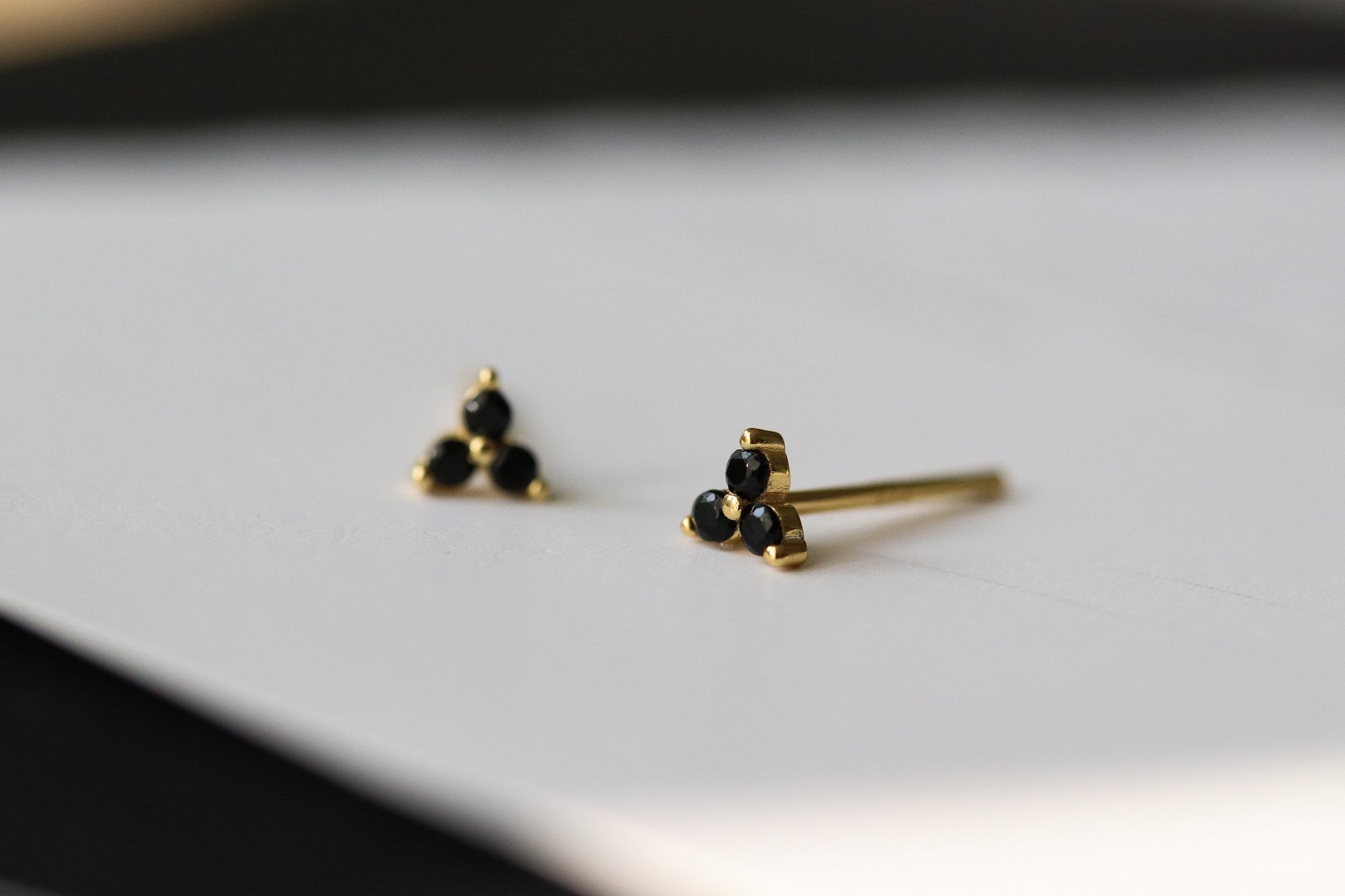 Shan&Co's Gold Vermeil CZ Black Shamrock Stud Earrings featuring a crystal black in a shamrock design, paired with Black Three Dot Earrings and Dainty Gold Trinity Leaf Earrings, blending elegance with nature-inspired charm in high-quality gold vermeil.