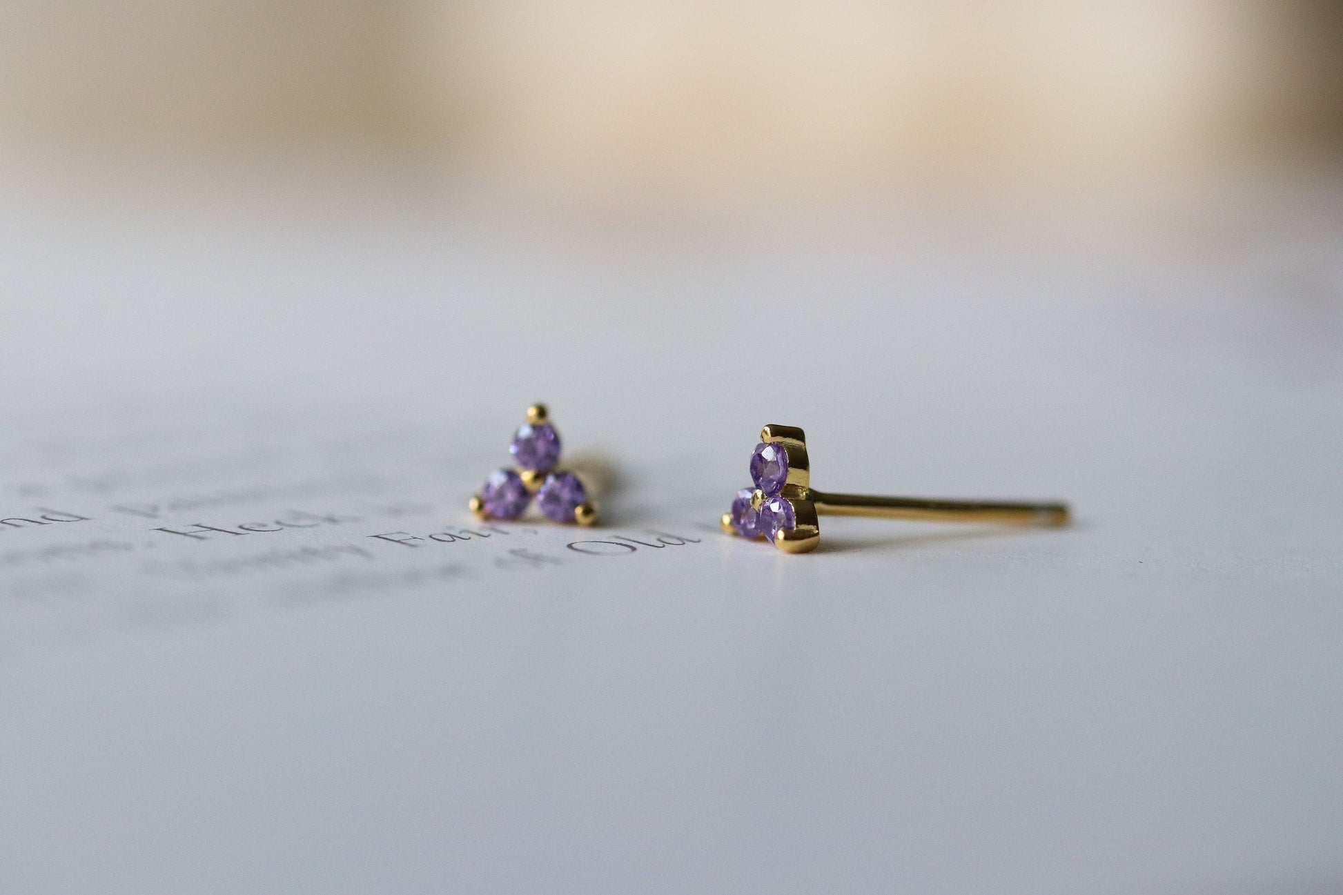 Shan&Co's Gold Vermeil CZ Lilac Shamrock Stud Earrings featuring a crystal lilac in a shamrock design, paired with LIlac Three Dot Earrings and Dainty Gold Trinity Leaf Earrings, blending elegance with nature-inspired charm in high-quality gold vermeil.