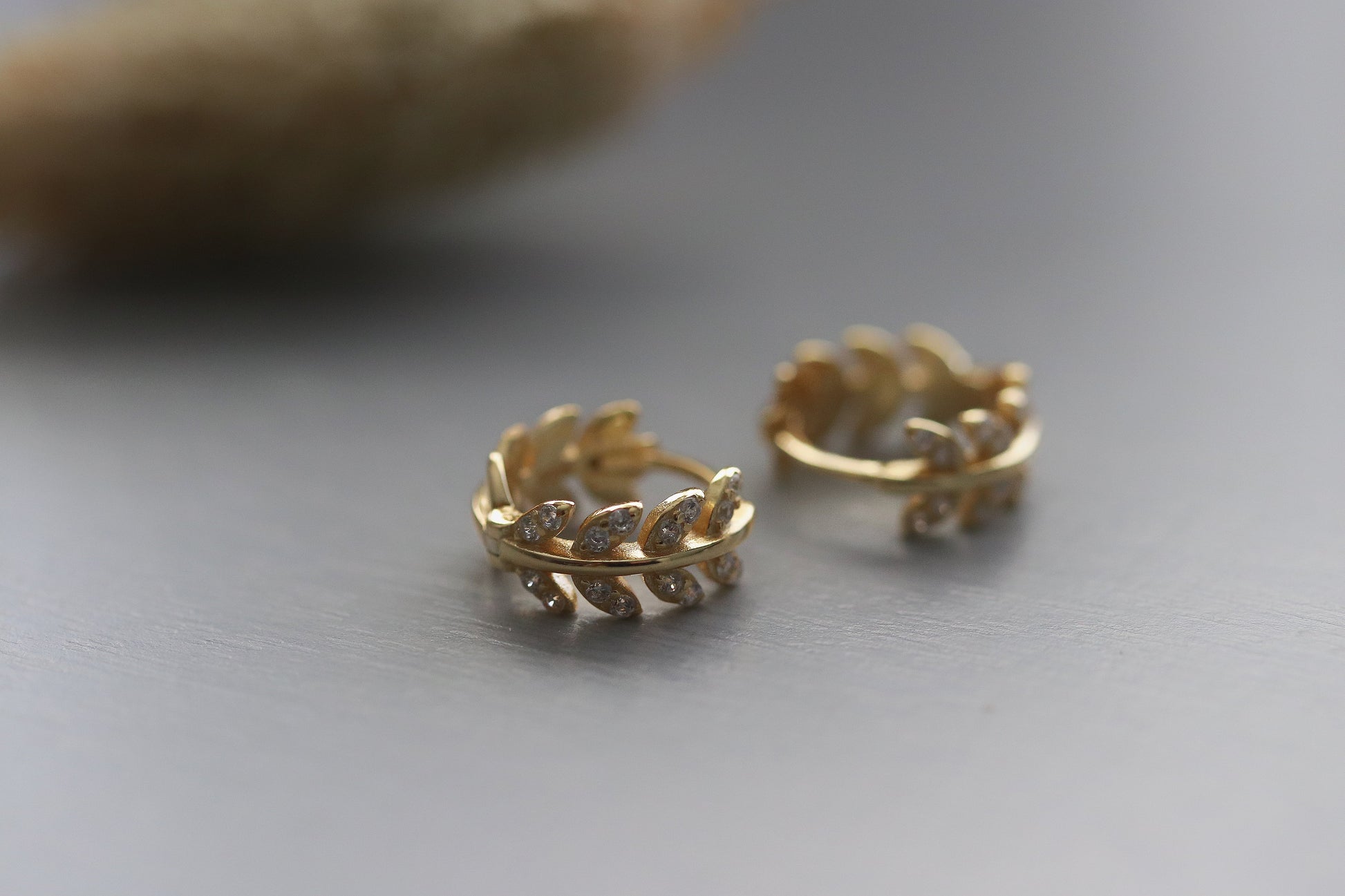 Shan&Co's Sterling Silver/Gold Vermeil CZ Olive Leaf Huggie Earrings, featuring a delicate olive leaf design with sparkling cubic zirconia, perfect for adding a nature-inspired touch of elegance to any outfit.