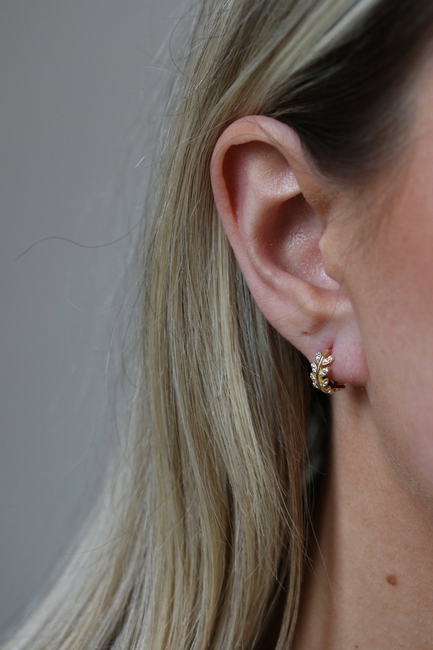 Shan&Co's Sterling Silver/Gold Vermeil CZ Olive Leaf Huggie Earrings, featuring a delicate olive leaf design with sparkling cubic zirconia, perfect for adding a nature-inspired touch of elegance to any outfit.