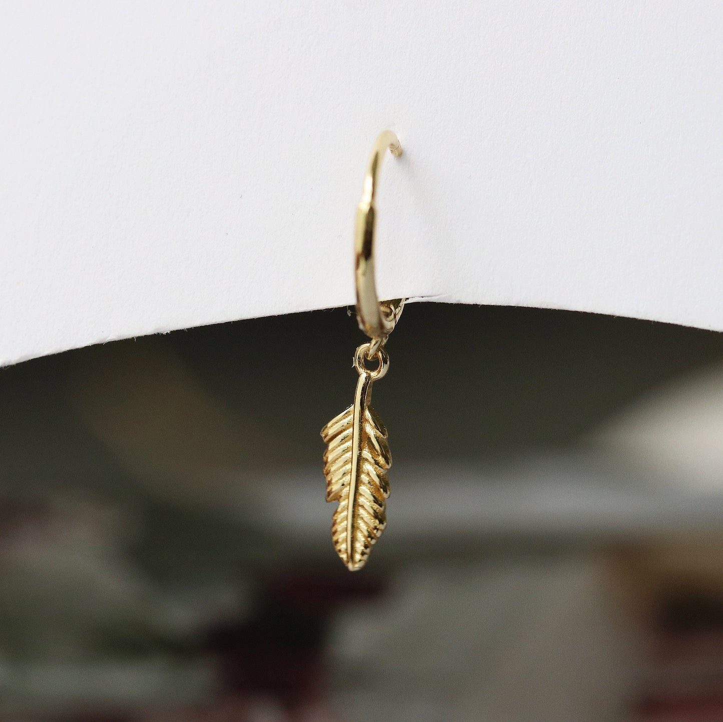 Shan&Co's Gold Feather Hoop Earrings featuring delicate feather charms, crafted from high-quality gold vermeil perfect for adding a light, bohemian touch to any outfit.