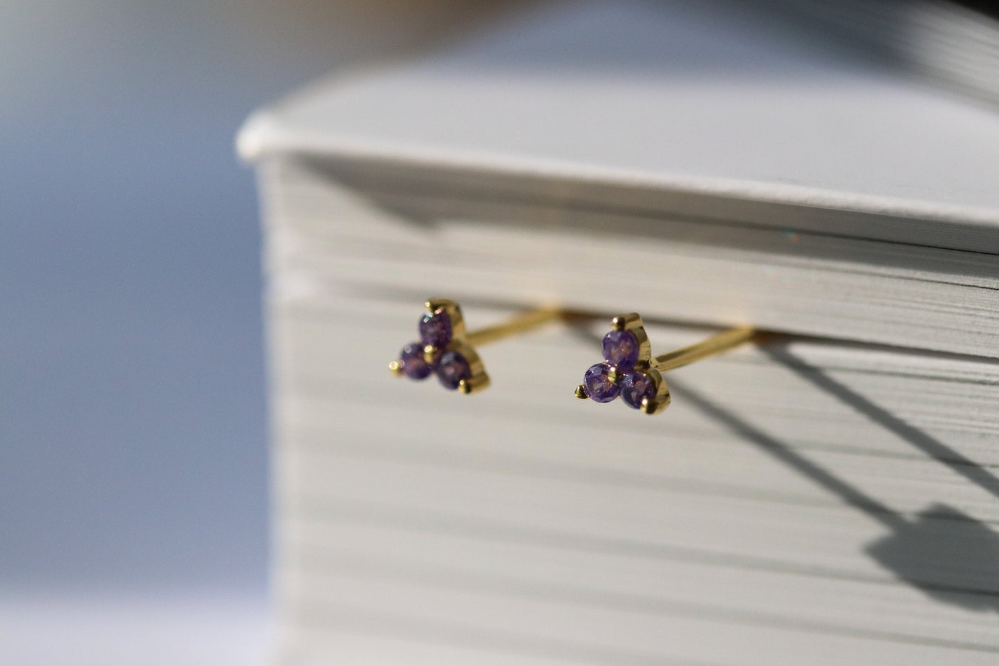 Shan&Co's Gold Vermeil CZ Lilac Shamrock Stud Earrings featuring a crystal lilac in a shamrock design, paired with Lilac Three Dot Earrings and Dainty Gold Trinity Leaf Earrings, blending elegance with nature-inspired charm in high-quality gold vermeil.