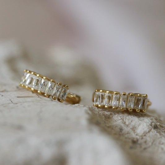  Shan&Co's Gold Plated Clear Baguette Hoop Earrings featuring clear-colored baguette crystals set in luxurious gold plating, perfect for adding a bold and colorful touch to any outfit