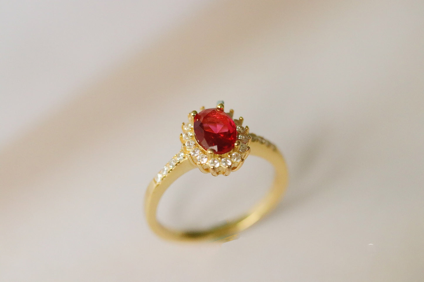 Gold Vermeil Ruby Halo Ring with CZ Accents featuring an elegant oval-cut red gemstone surrounded by a halo of sparkling cubic zirconia. Luxurious and durable, perfect for special occasions or everyday glamour.