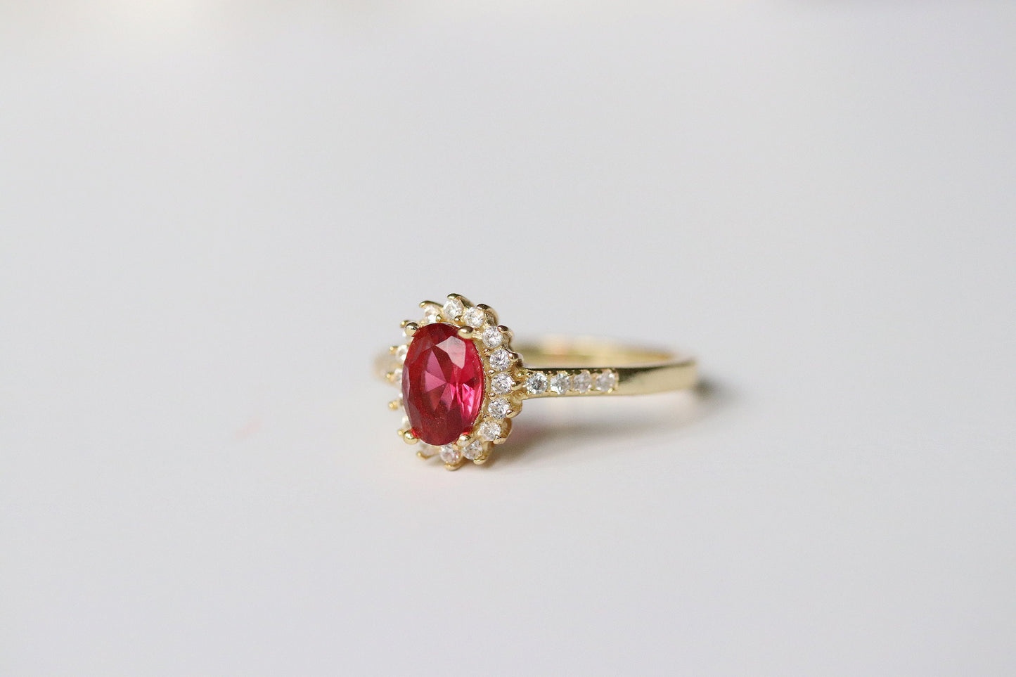 Gold Vermeil Ruby Halo Ring with CZ Accents featuring an elegant oval-cut red gemstone surrounded by a halo of sparkling cubic zirconia. Luxurious and durable, perfect for special occasions or everyday glamour.