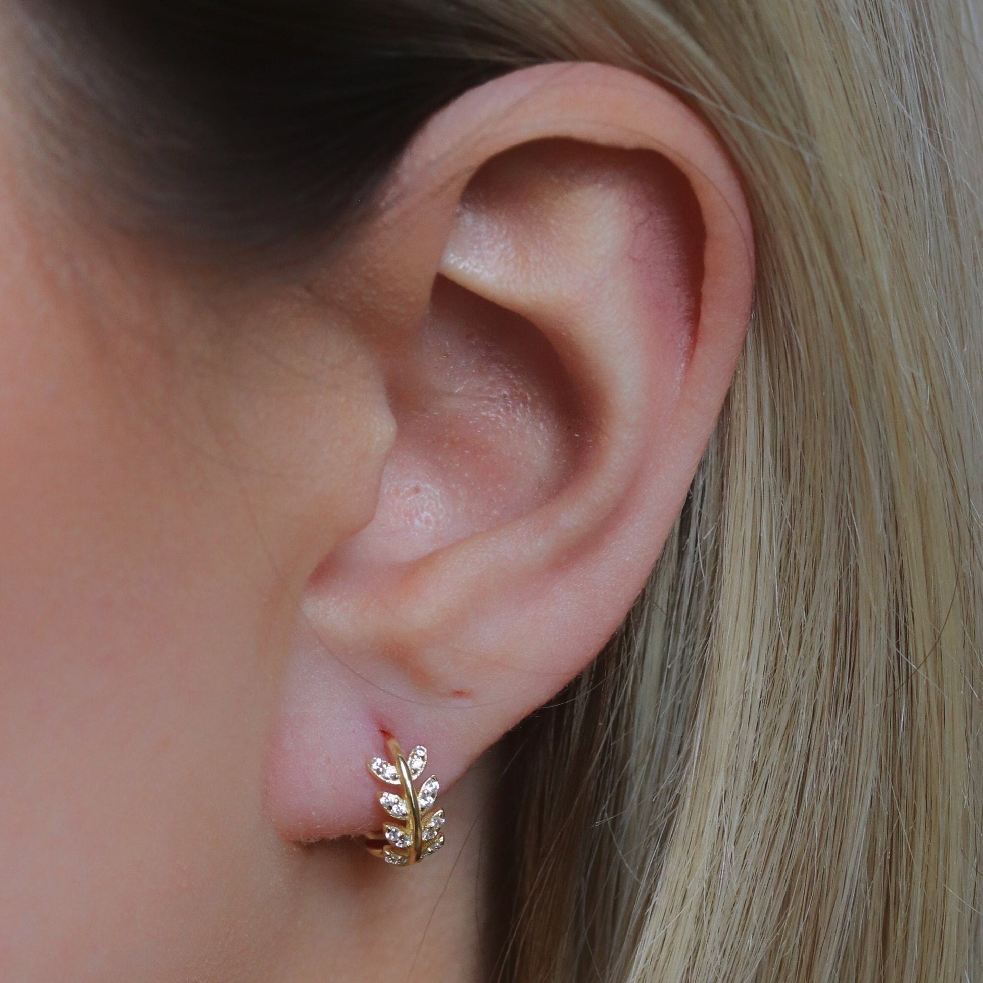 Shan&Co's Sterling Silver/Gold Vermeil CZ Olive Leaf Huggie Earrings, featuring a delicate olive leaf design with sparkling cubic zirconia, perfect for adding a nature-inspired touch of elegance to any outfit.