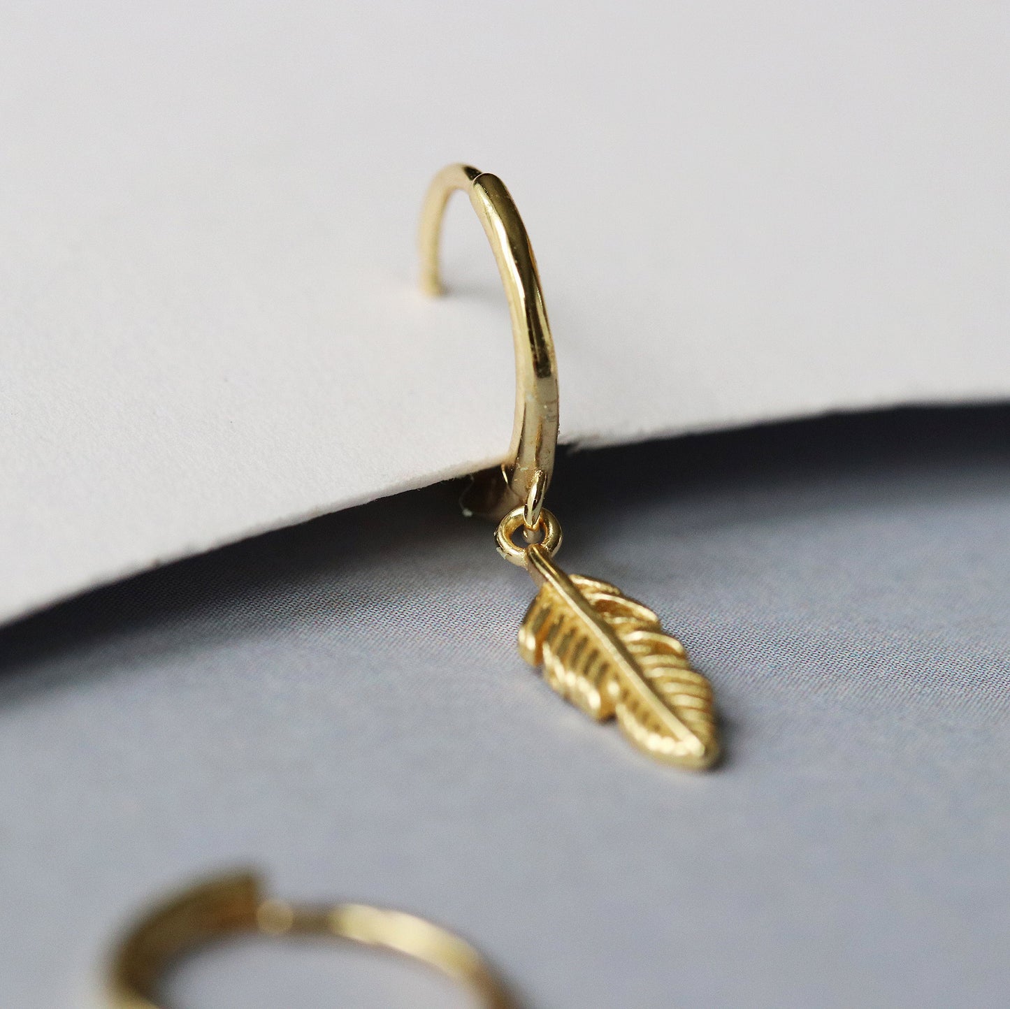 Shan&Co's Sterling Gold Feather Hoop Earrings featuring delicate feather charms, crafted from high-quality gold vermeil perfect for adding a light, bohemian touch to any outfit.