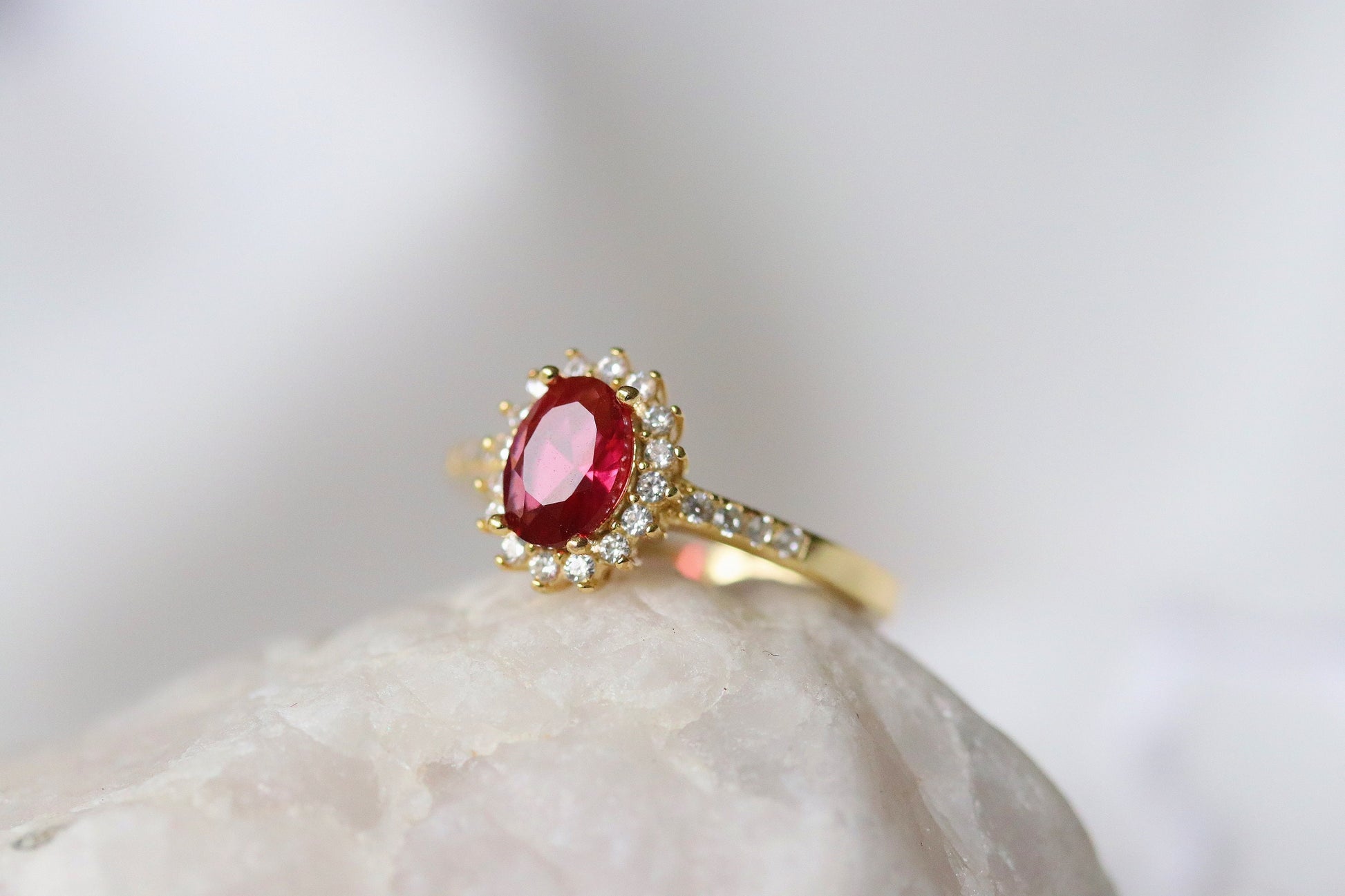 Gold Vermeil Ruby Halo Ring with CZ Accents featuring an elegant oval-cut red gemstone surrounded by a halo of sparkling cubic zirconia. Luxurious and durable, perfect for special occasions or everyday glamour.