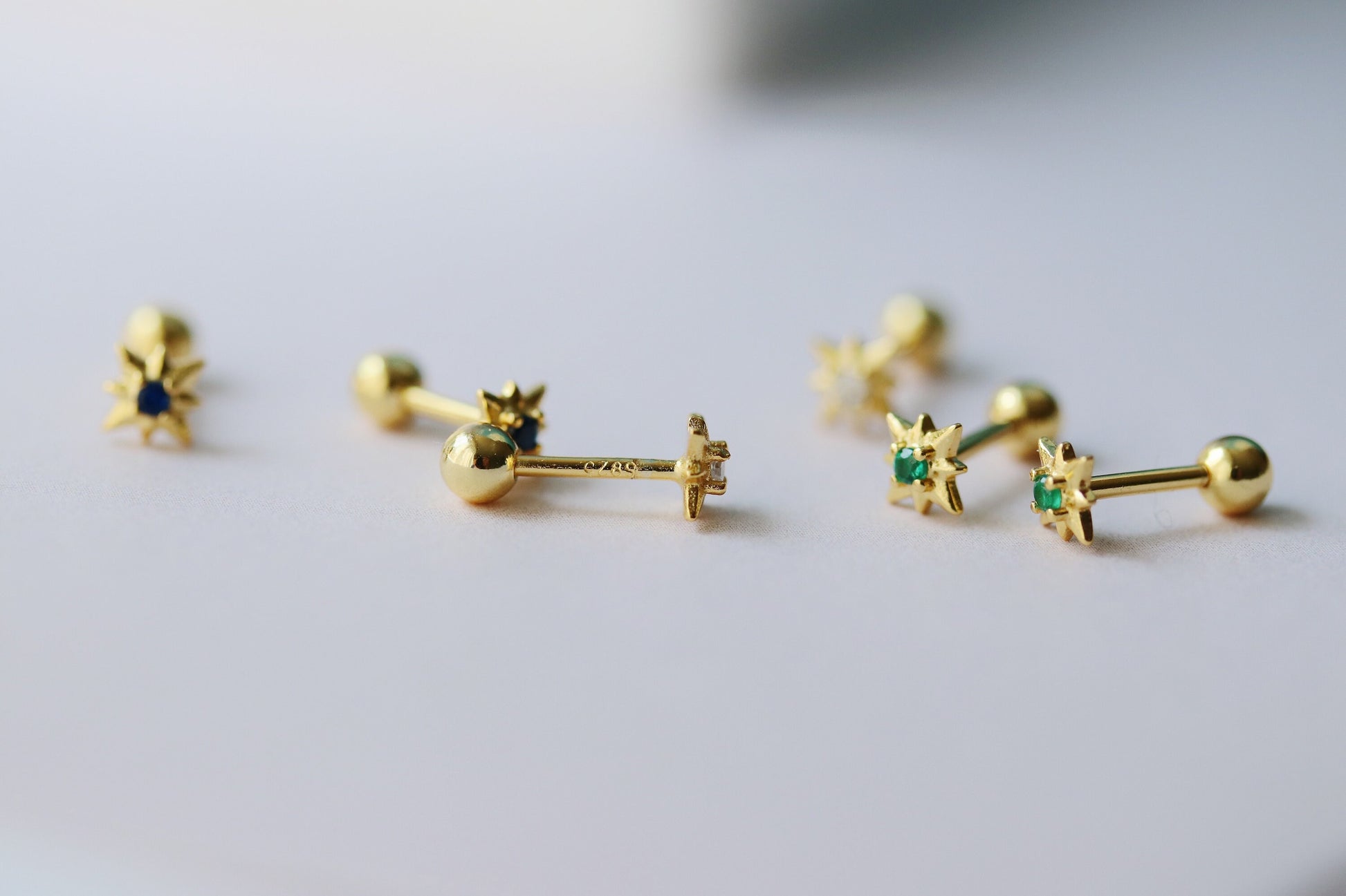 Shan&Co's Gold Starburst Screw Emerald Earrings featuring a radiant starburst design with vibrant emerald accents, paired with Star Barbell Earrings for a modern celestial look, crafted in high-quality gold.