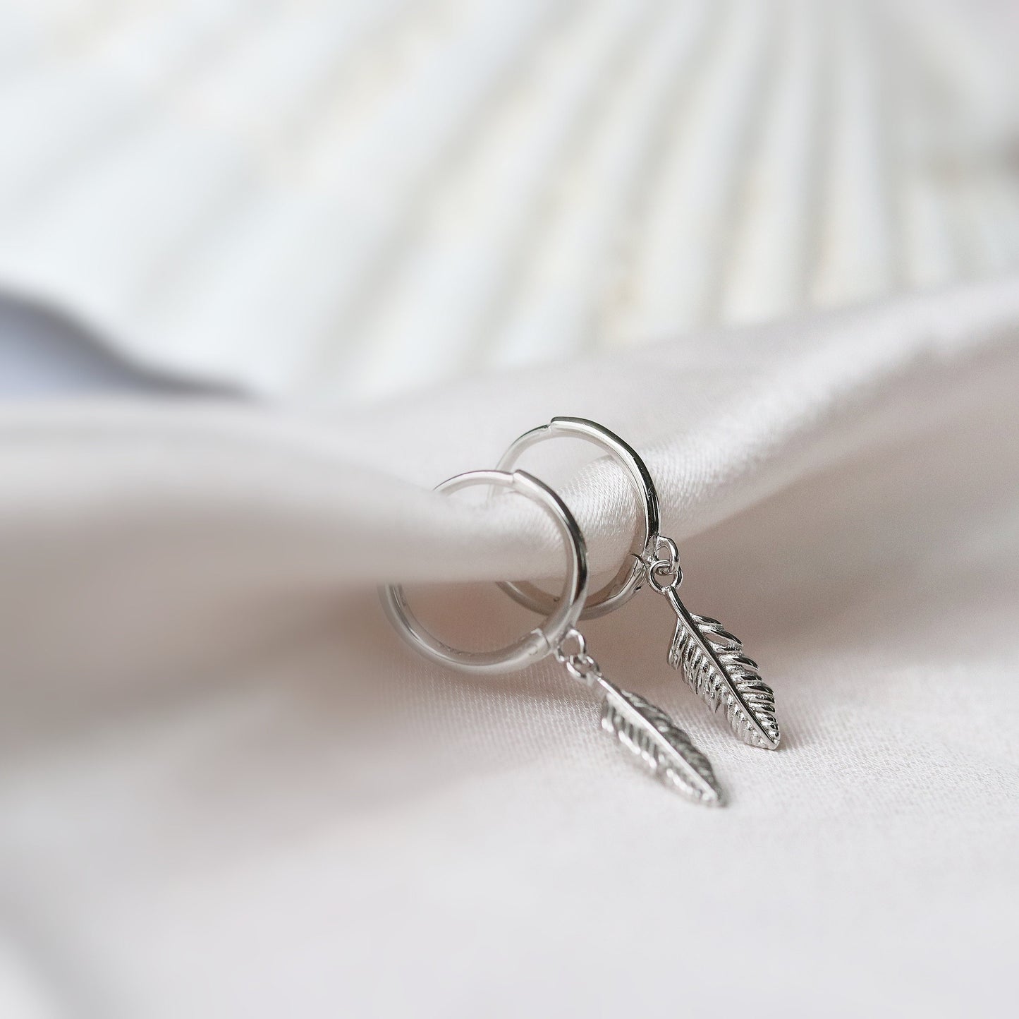 Shan&Co's Sterling Silver Feather Hoop Earrings featuring delicate feather charms, crafted from high-quality sterling silver, perfect for adding a light, bohemian touch to any outfit.